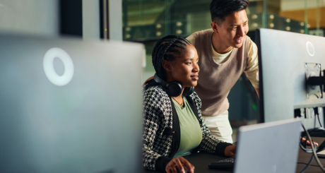 A woman and man look at a computer monitor in an office setting.